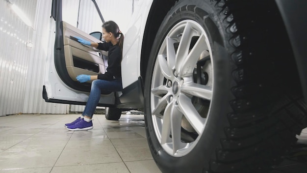 Mulher jovem com luvas azuis limpando o interior do carro para um SUV de luxo, close-up