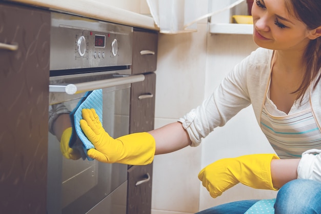 Mulher jovem com luvas de borracha limpando a cozinha