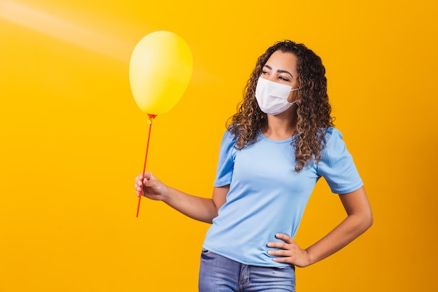 Mulher jovem com máscara cirúrgica, segurando um balão amarelo.