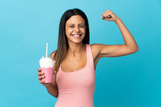 Mulher jovem com milk-shake de morango fazendo um gesto forte