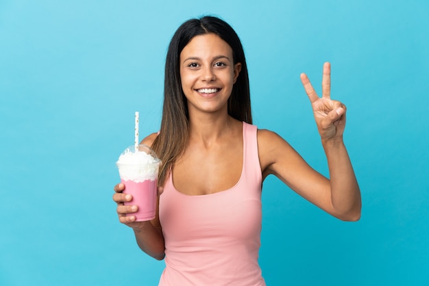 Mulher jovem com milk-shake de morango sorrindo e mostrando sinal de vitória