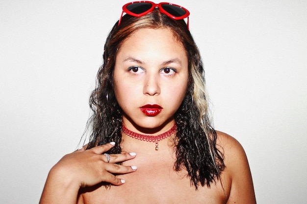 Mulher jovem com óculos de sol usando colar de garganta e batom vermelho contra fundo cinza