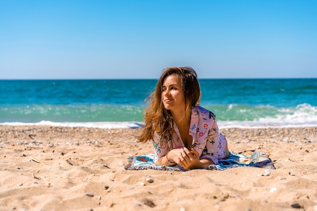 Mulher jovem com óculos escuros e vestido deitada na praia em frente ao mar