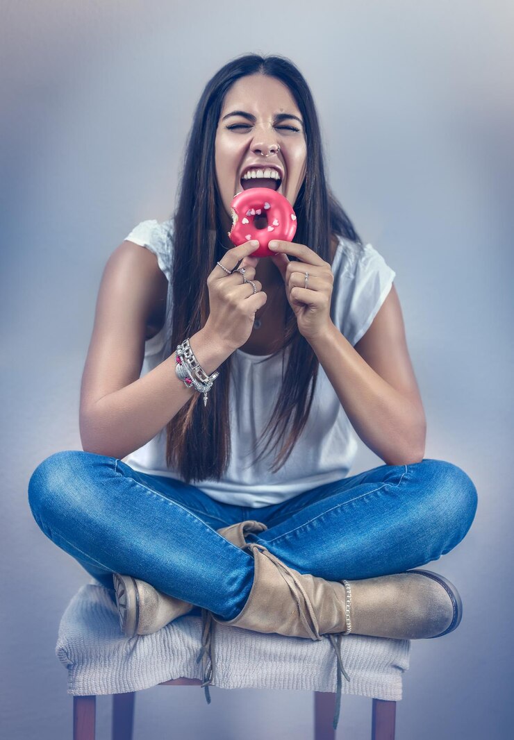 Foto mulher jovem com os olhos fechados comendo donut enquanto sentada contra a parede