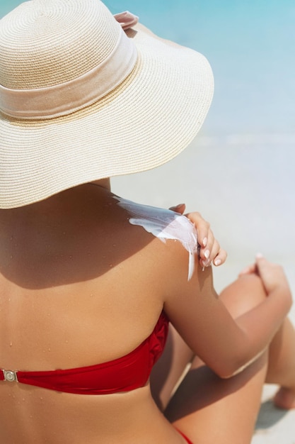 Mulher jovem com pele saudável aplicando proteção solar nas costas bronzeadas