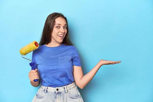 Mulher jovem com rolo de pintura amarelo em um fundo azul mostrando um espaço de cópia em uma palma