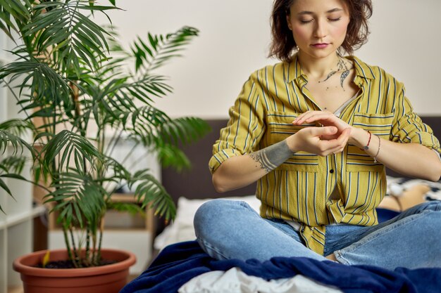 Mulher jovem com roupa casual sentada na cama, relaxando na pose de lótus de ioga, fazendo meditação em casa