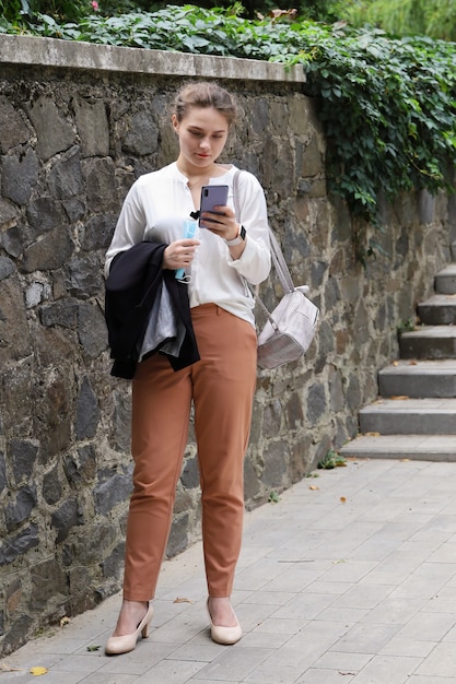 Mulher jovem com roupa de negócios segura o smartphone e olha para a tela no parque