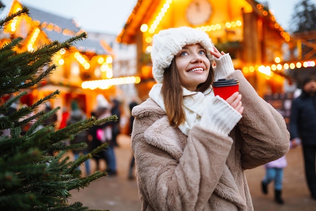 Mulher jovem com roupas de estilo de inverno posando no mercado de rua festivo Mulher desfrutando de momentos de inverno