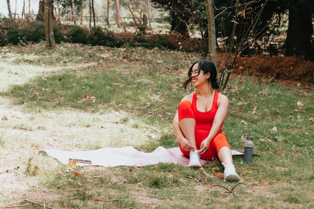 Mulher jovem com roupas de ginástica, descansando sobre um tapete de ioga no parque
