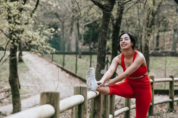 Mulher jovem com roupas de ginástica, esticando o corpo no parque enquanto sorri