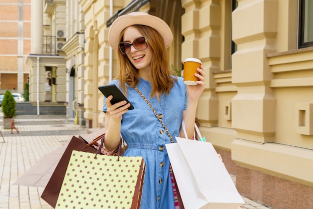 Mulher jovem com sacolas de compras andando por uma cidade em dia de verão