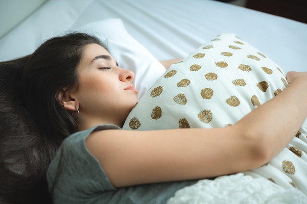 Foto mulher jovem com sono relaxando no sofá em casa, estilo de vida confortável de menina, mulher bonita feliz em descansar no quarto de cama, lazer e pessoa calma deitada com um travesseiro branco pela manhã, pessoas