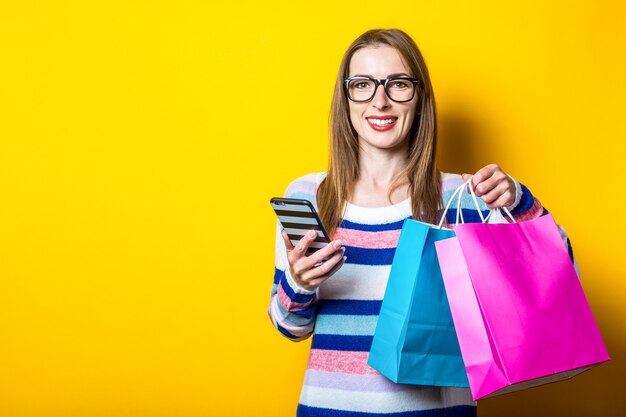 Mulher jovem com suéter segurando sacolas de compras e celular