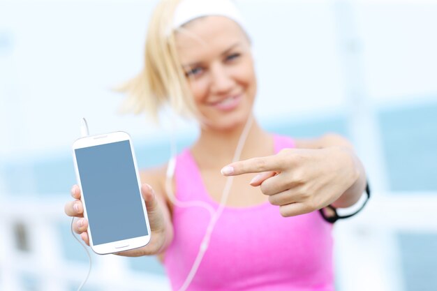 Mulher jovem com sutiã esportivo rosa mostrando o telefone sobre o mar