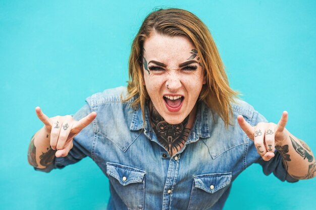 Mulher jovem com tatuagens gritando e fazendo sinal de rock n roll