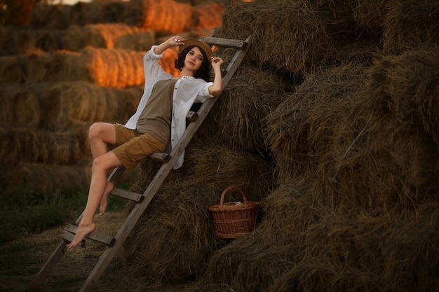 Mulher jovem com um chapéu de palha em estilo rústico sentada descansando no campo em uma velha escada de madeira