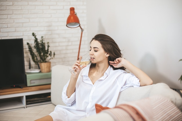 Mulher jovem com um copo de vinho em casa. A pessoa do sexo feminino relaxa bebendo vinho.