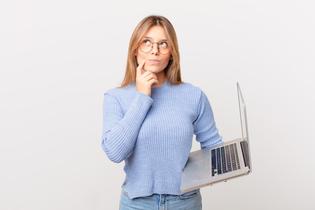 Mulher jovem com um laptop pensando, se sentindo em dúvida e confusa