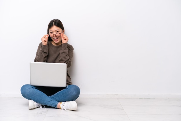 Mulher jovem com um laptop sentada no chão com óculos e surpresa