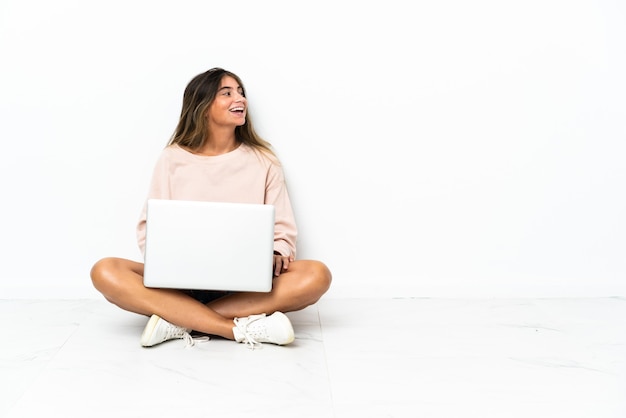 Mulher jovem com um laptop sentada no chão isolada