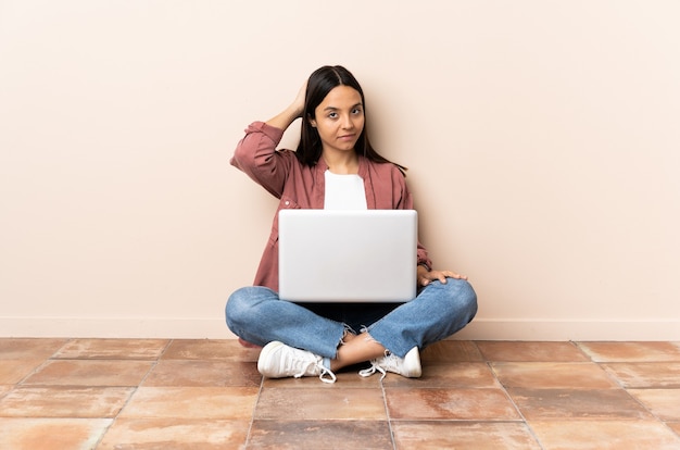 Mulher jovem com um laptop sentada no chão, nas costas e pensando