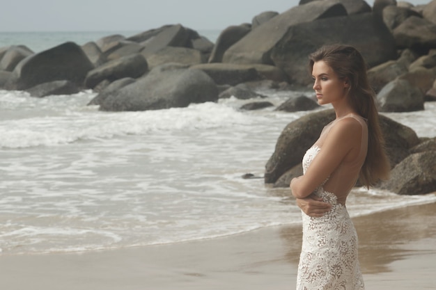 Mulher jovem com um lindo vestido branco posando na praia rochosa