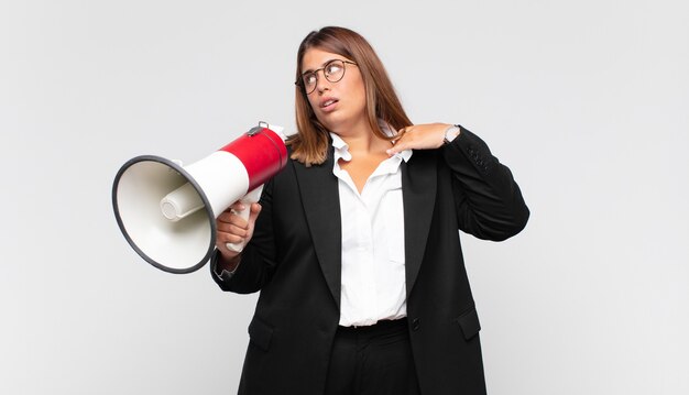 Mulher jovem com um megafone se sentindo estressada, ansiosa, cansada e frustrada, puxando o pescoço da camisa, parecendo frustrada com o problema