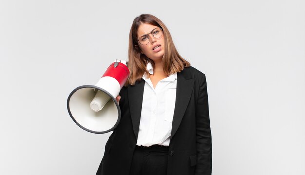 Mulher jovem com um megafone se sentindo perplexa e confusa, com uma expressão muda e atordoada olhando para algo inesperado