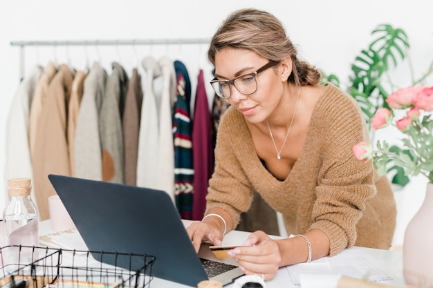 Mulher jovem com um pulôver de lã bege casual olhando para a tela do laptop enquanto faz pedidos na loja online