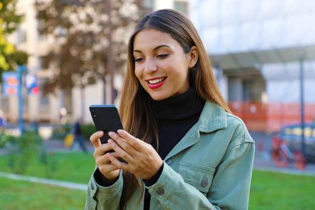 Mulher jovem com um smartphone conversando ao ar livre no outono ou inverno