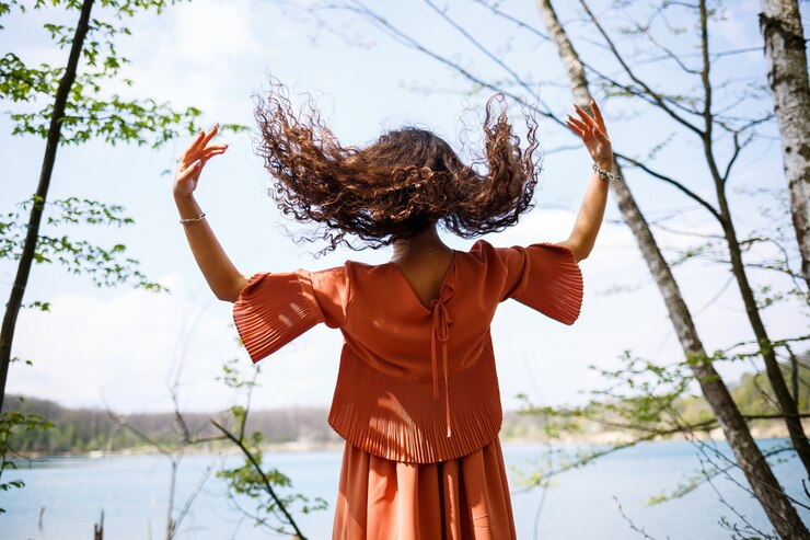 Foto mulher jovem com um sorriso no rosto, emoções felizes. uma garota com longos cabelos ondulados e encaracolados em um vestido no verão na natureza, em uma floresta em um lago, estava perto de uma estrada e arbustos