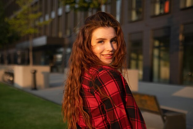 Mulher jovem com um sorriso radiante e cabelo vermelho está contra o pano de fundo de um centro de negócios