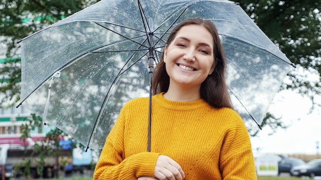 Mulher jovem com um suéter mostarda sob um guarda-chuva transparente no tempo chuvoso