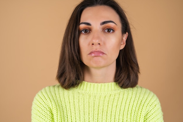 Mulher jovem com um suéter verde claro em uma parede bege fofa chateada com um olhar triste, desapontada