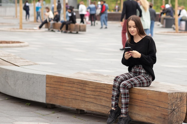 Mulher jovem com um telefone na rua em um banco sorrindo