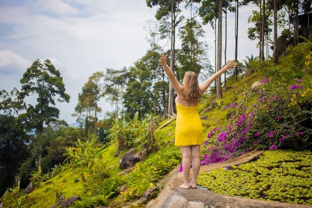 Foto mulher jovem com um vestido abriu os braços em frente à vista traseira de uma floresta tropical