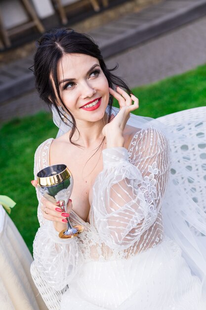 Mulher jovem com um vestido branco, segurando uma taça de champanhe na luz do sol. Conceito de festa ao ar livre.