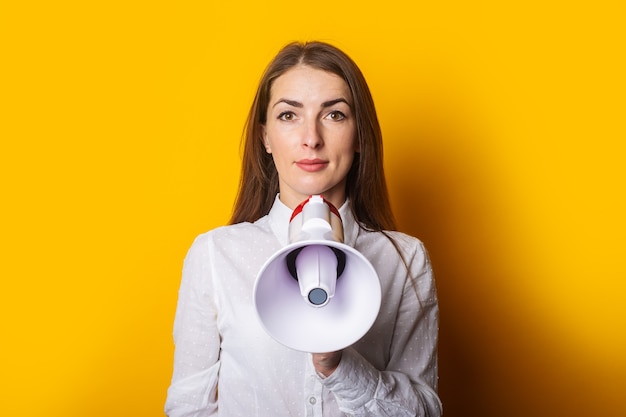 Mulher jovem com uma camisa branca segurando um megafone em um fundo amarelo