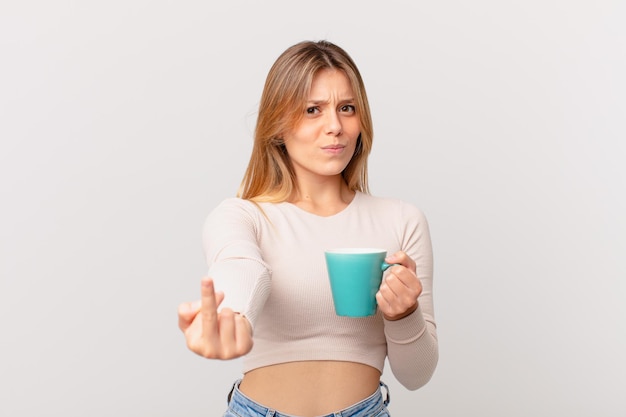 Mulher jovem com uma caneca de café se sentindo irritada, irritada, rebelde e agressiva