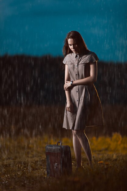 Mulher jovem com uma mala parada sob chuva e esperando