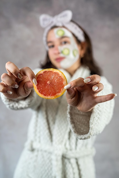 mulher jovem com uma máscara de barro e pepinos de toranja procedimento cosmético cuidado da pele e limpo