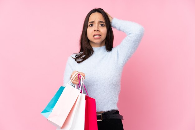 Mulher jovem com uma sacola de compras sobre um fundo rosa isolado frustrada e leva as mãos na cabeça