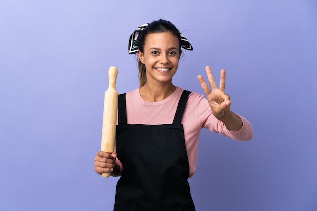 Mulher jovem com uniforme de chef feliz e contando três com os dedos