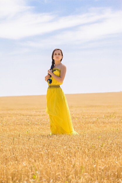 Mulher jovem com vestido amarelo em campo de trigo