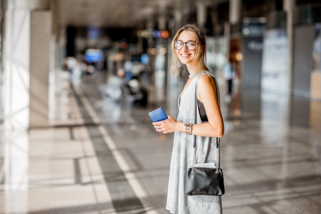 Mulher jovem com vestido cinza em pé com cartões de embarque no saguão de embarque do aeroporto esperando o voo