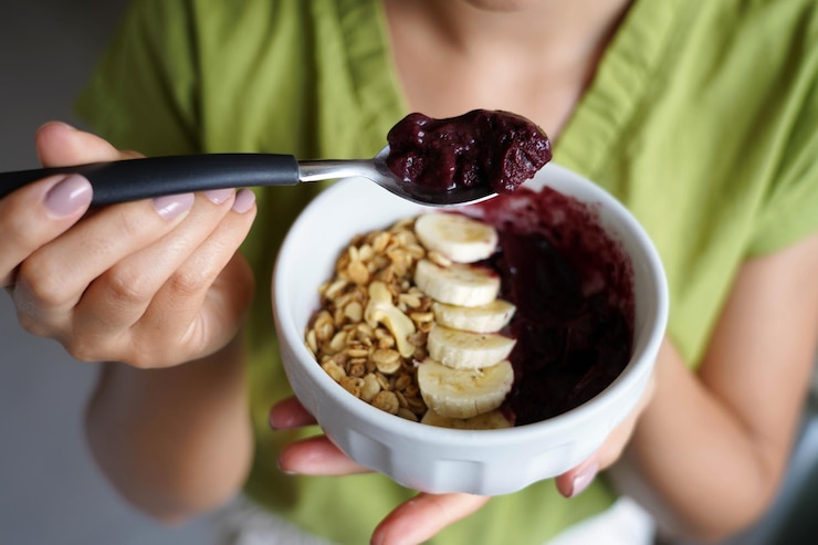 Foto mulher jovem comendo acai brasileiro de uma tigela com banana e granola como café da manhã