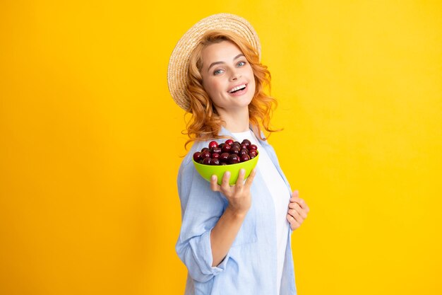 Foto mulher jovem comendo cerejas doces retrato de uma menina bonita com cereja em fundo amarelo estação de colheita de frutas de verão vitaminas naturais