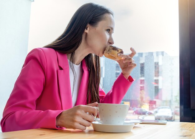 Mulher jovem comendo donut com xícara de café Conceito de comer pobre