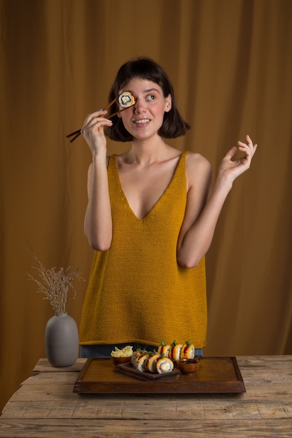 Mulher jovem comendo e saboreando um rolo de sushi fresco usando os pauzinhos